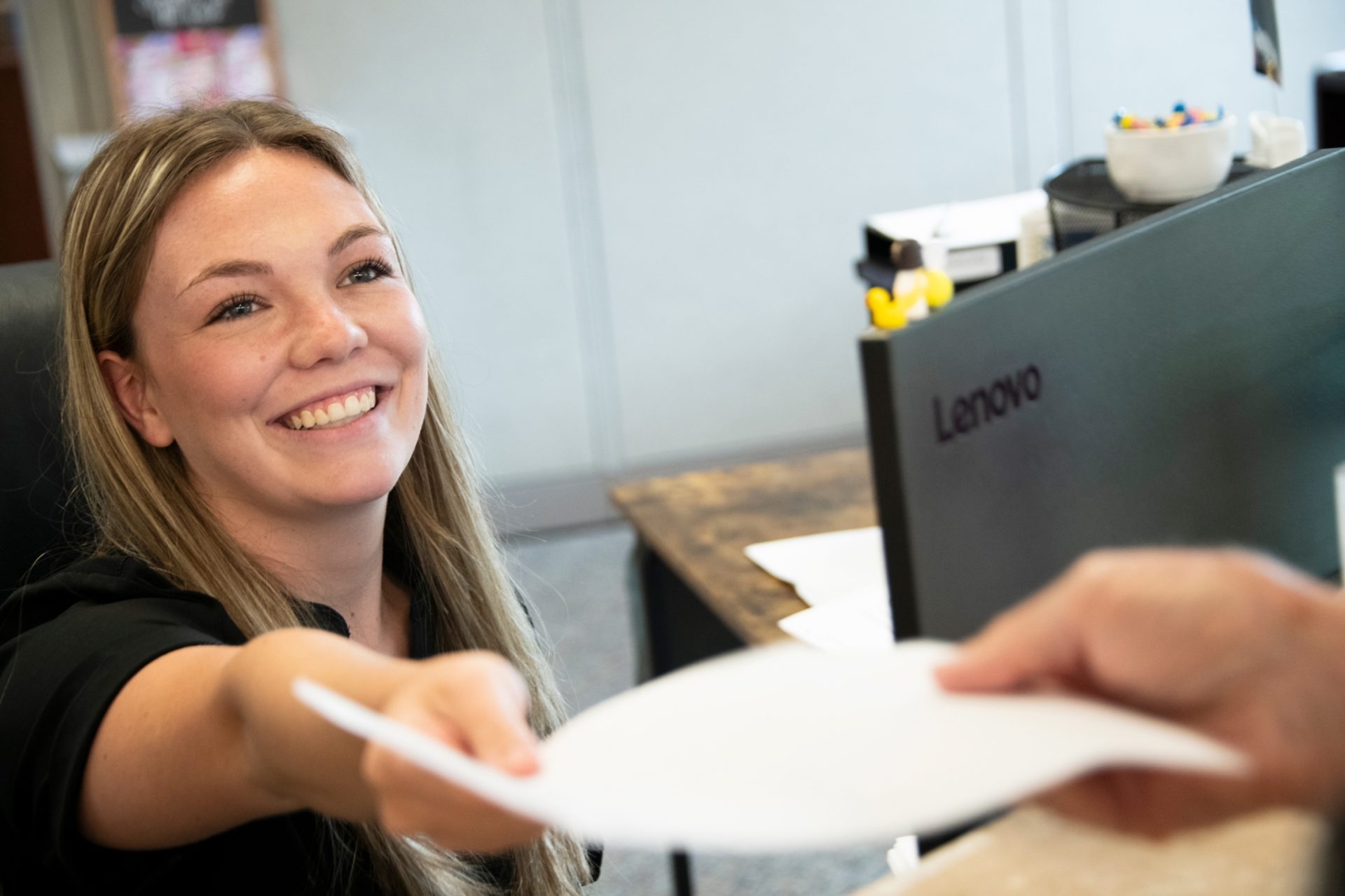 Receptionist smiling while handing check-in documents to a patient at a Mississippi kidney nephrology office.