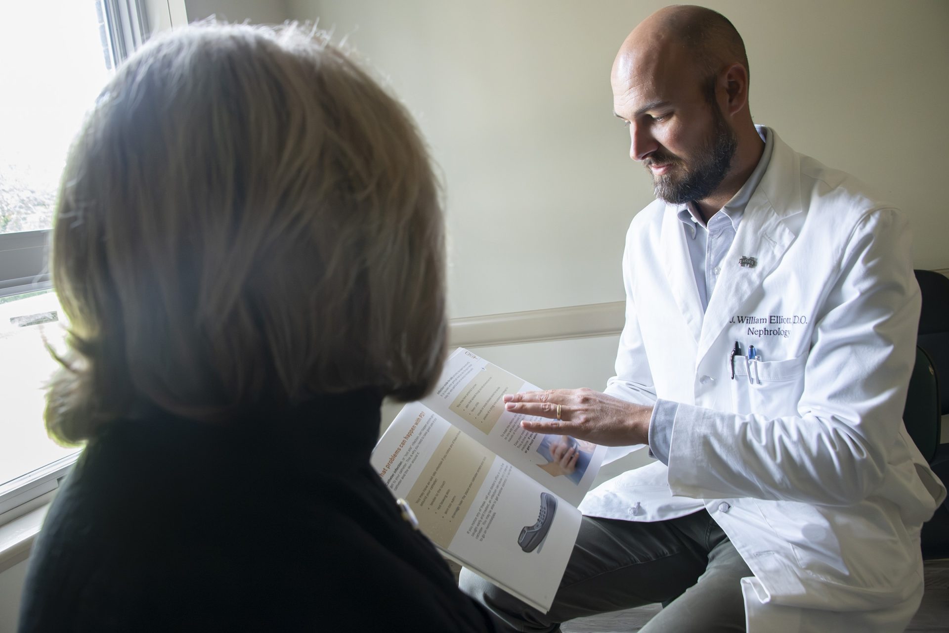 Nephrologist Dr. Elliott reviewing an educational booklet with a patient during a clinic appointment.