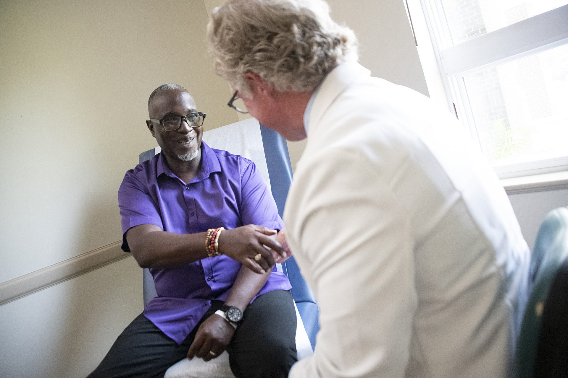 Smiling male patient shaking hands with a nephrologist in a medical exam room.