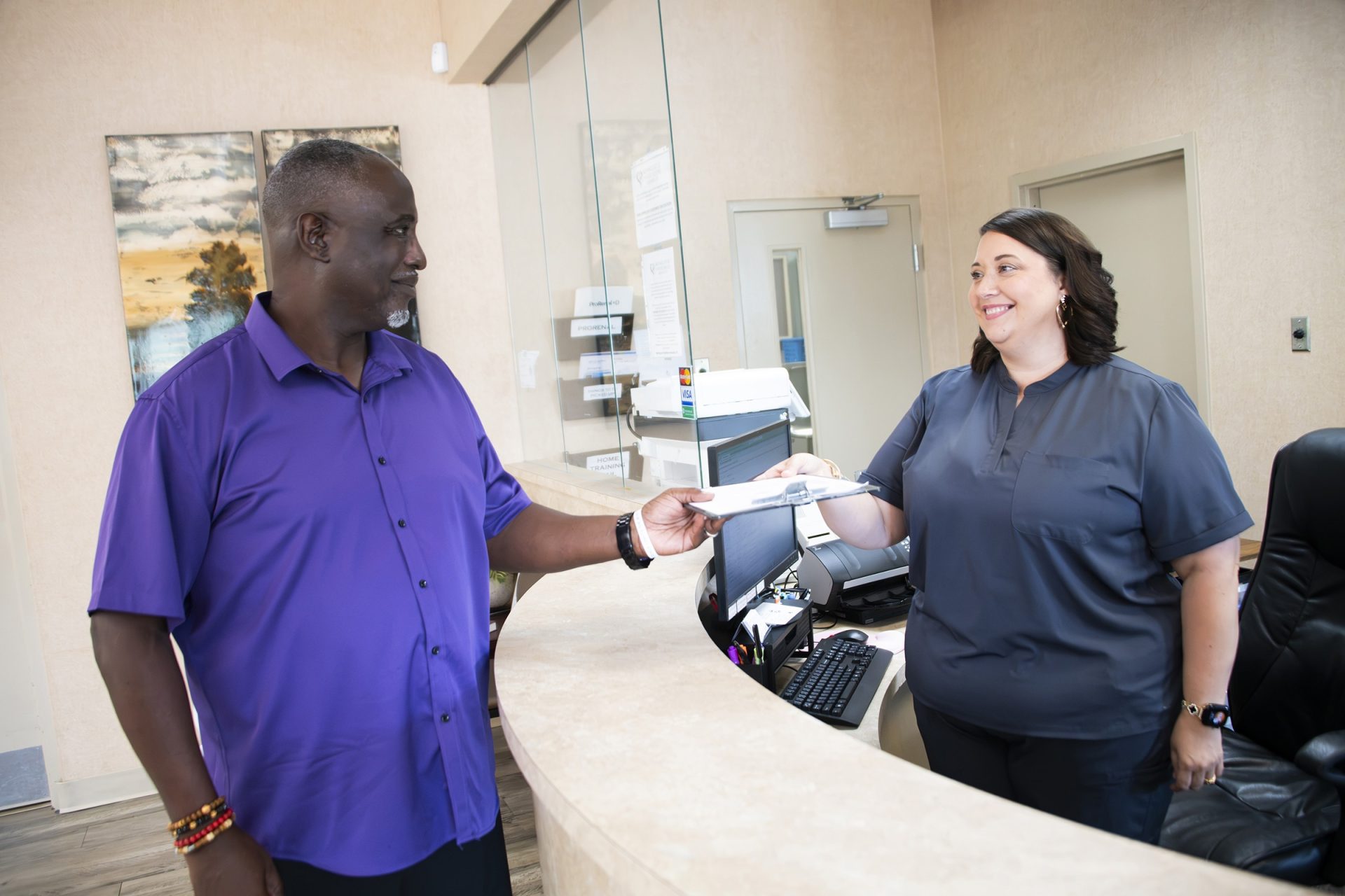 Male patient handing intake paperwork to a receptionist at the front desk of a Mississippi kidney nephrology clinic.