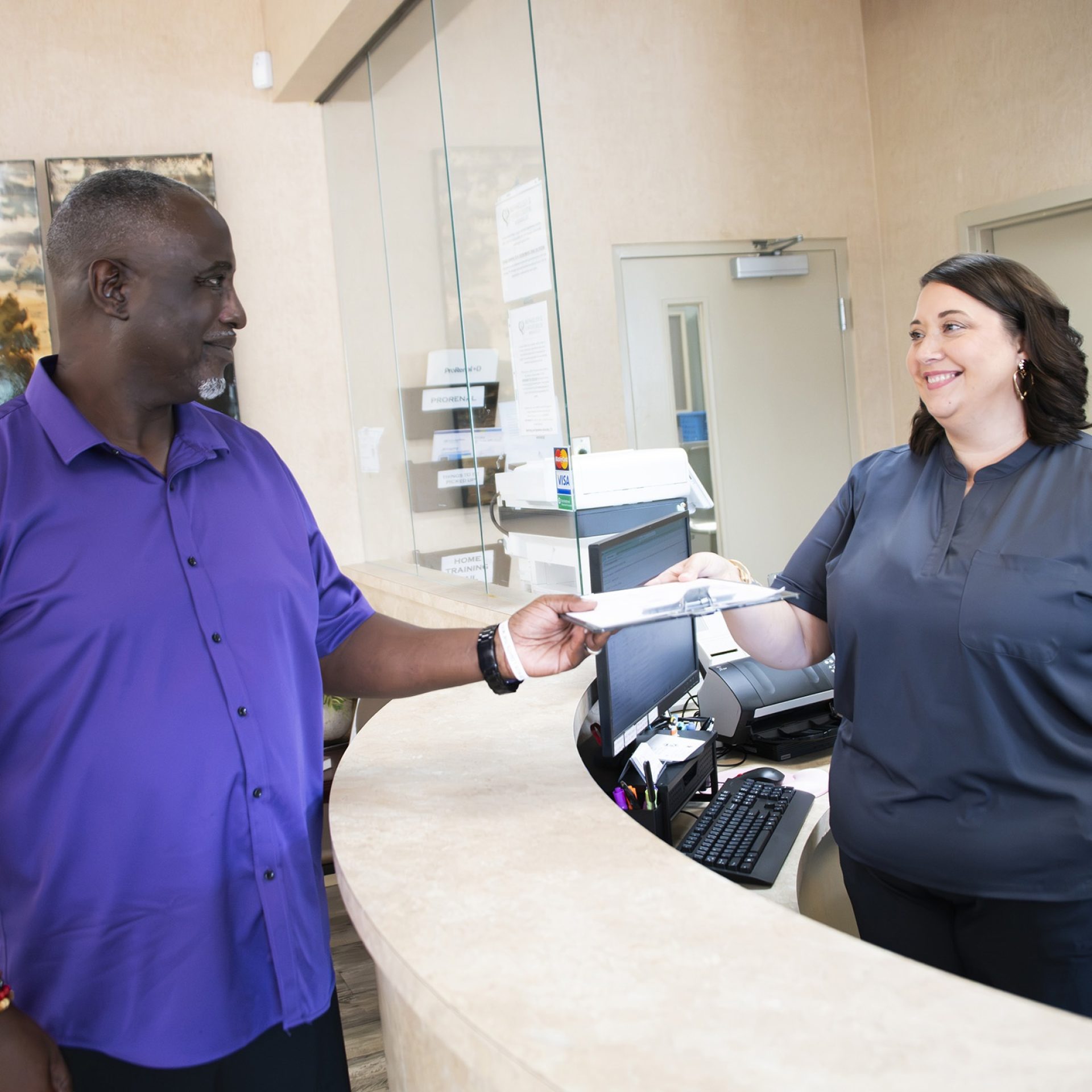 Male patient handing intake paperwork to a receptionist at the front desk of a Mississippi kidney nephrology clinic.